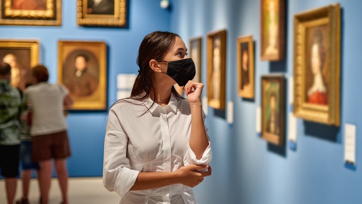 Woman visitor wearing an antivirus mask in the historical museum looking at pictures.